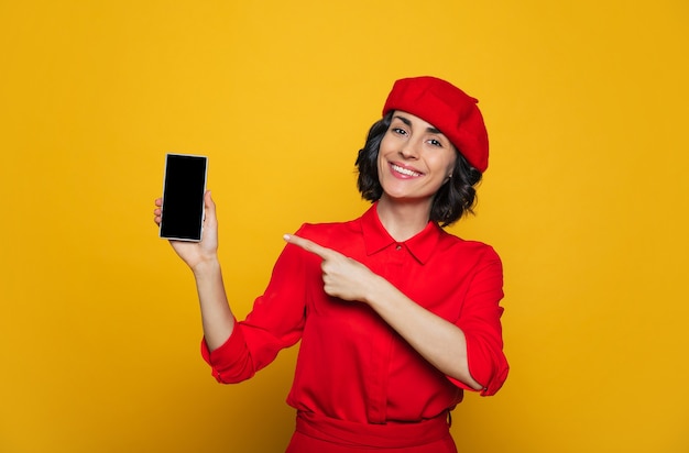 jolie femme française, vêtue d'un style parisien, avec un béret rouge, pointe sur son smartphone.