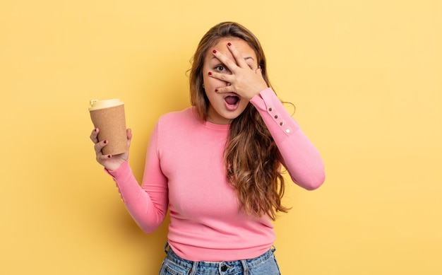 Jolie femme hispanique à l'air choquée, effrayée ou terrifiée, couvrant le visage avec la main. concept de café à emporter