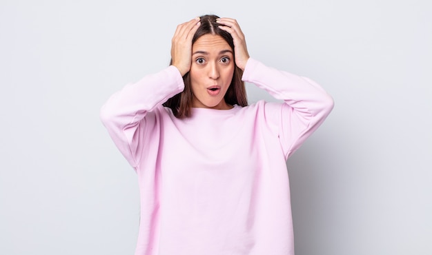 Jolie femme hispanique à l'air excitée et surprise, bouche bée avec les deux mains sur la tête, se sentant comme une heureuse gagnante