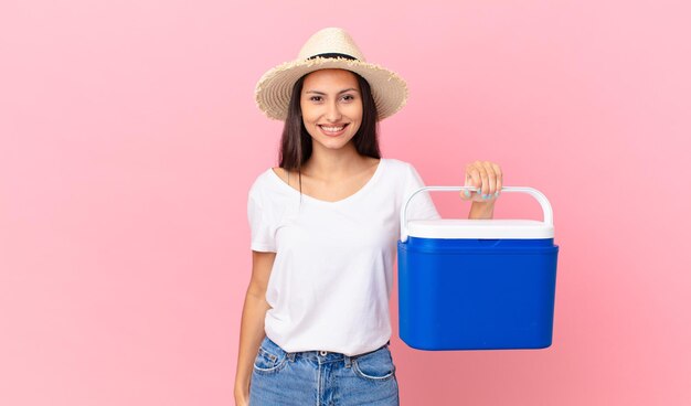 jolie femme hispanique à l'air heureuse et agréablement surprise et tenant un réfrigérateur portable