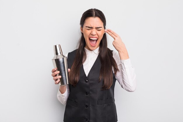 jolie femme hispanique à l'air malheureuse et stressée, geste de suicide faisant signe d'arme à feu. concept de cocktail de barman