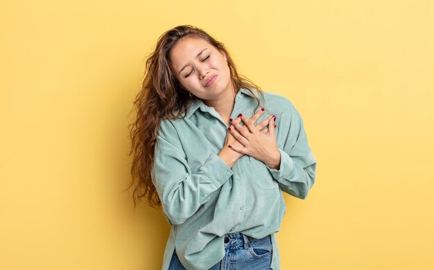 Jolie femme hispanique à l'air triste, blessée et navrée, tenant les deux mains près du cœur, pleurant et se sentant déprimée