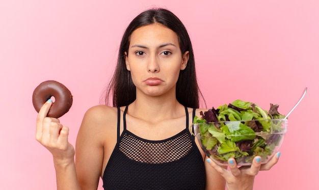 Jolie femme hispanique avec un beignet et une salade. concept de régime