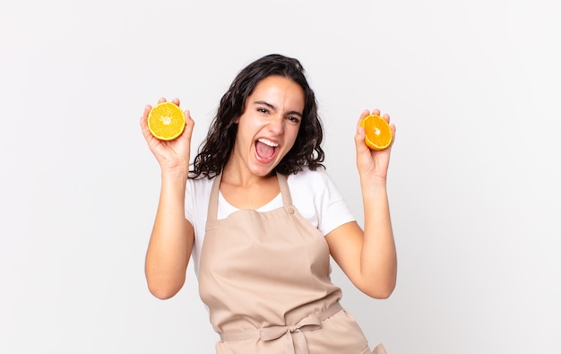 Jolie femme hispanique de chef préparant un jus d'orange