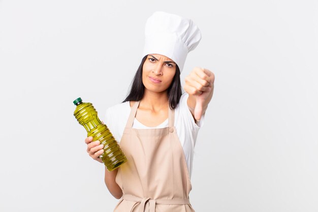 Jolie femme hispanique chef tenant une bouteille d'huile d'olive.