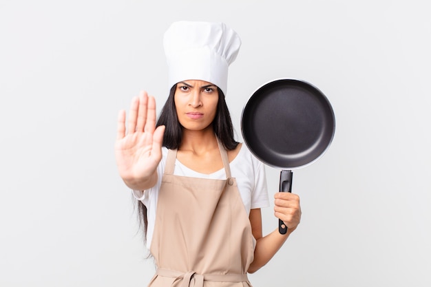 Jolie femme hispanique de chef tenant une casserole