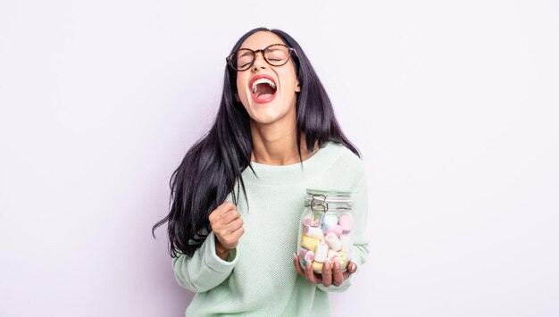 Jolie femme hispanique criant agressivement, regardant le concept de bonbons à la gelée très en colère