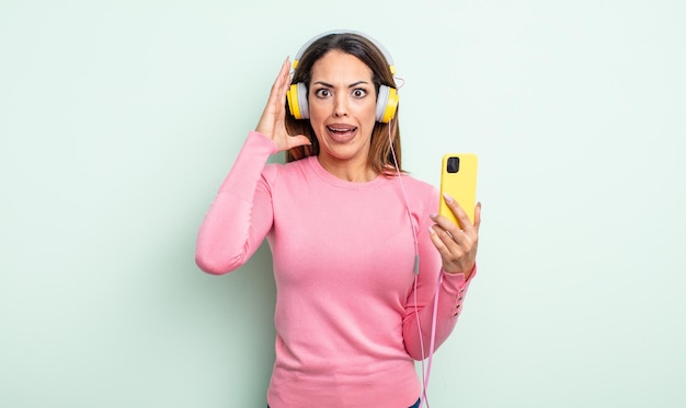 Jolie femme hispanique criant avec les mains en l'air. concept de smartphone et d'écouteurs