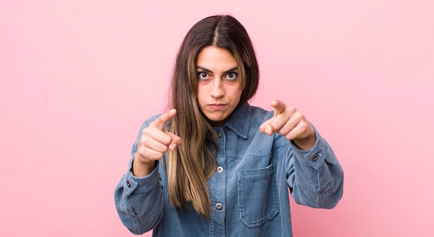 Jolie femme hispanique pointant vers l'avant à la caméra avec les deux doigts et une expression de colère vous disant de faire votre devoir