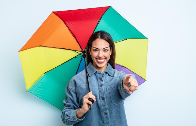 Jolie femme hispanique pointant vers la caméra en vous choisissant. concept de parapluie