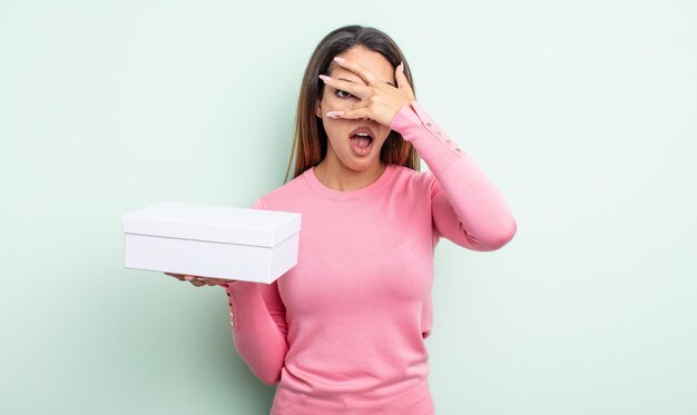 Jolie femme hispanique qui a l'air choquée, effrayée ou terrifiée, couvrant le visage avec la main. concept d'emballage de boîte blanche