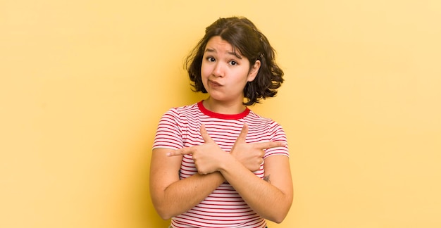 Jolie femme hispanique qui a l'air perplexe et confuse, peu sûre et pointant dans des directions opposées avec des doutes