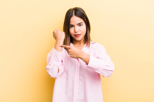 Jolie femme hispanique à la recherche d'impatience et de colère pointant vers la montre demandant la ponctualité veut être à l'heure