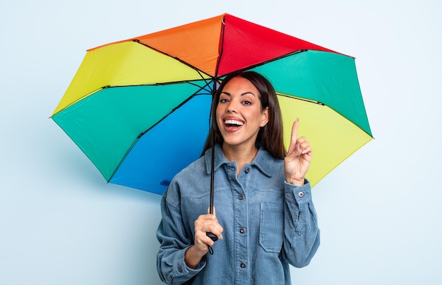 Jolie femme hispanique se sentant comme un génie heureux et excité après avoir réalisé une idée. concept de parapluie