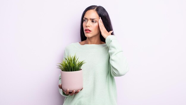 Jolie femme hispanique se sentant confuse et perplexe, montrant que vous êtes fou. concept de plante d'intérieur