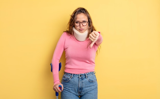 Jolie femme hispanique se sentant croisée, montrant les pouces vers le bas. accident de béquille et de collier