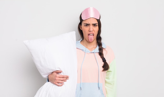 Jolie femme hispanique se sentant dégoûtée et irritée et tirant la langue. concept pyjama et oreiller
