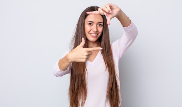 jolie femme hispanique se sentant heureuse, amicale et positive, souriante et faisant un portrait ou un cadre photo avec les mains