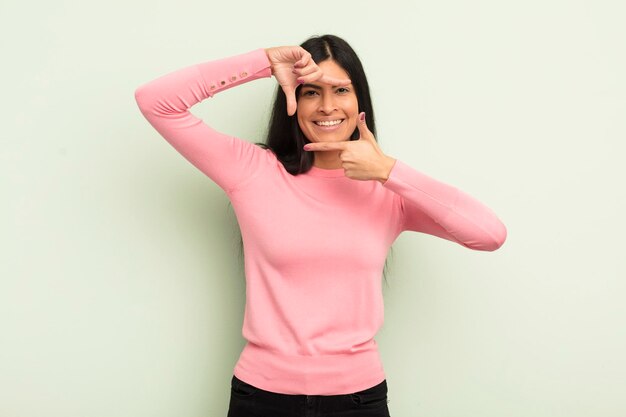 Jolie femme hispanique se sentant heureuse amicale et positive souriante et faisant un portrait ou un cadre photo avec les mains