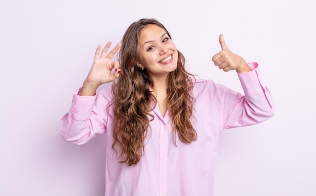 Jolie femme hispanique se sentant heureuse, étonnée, satisfaite et surprise, montrant d'accord et pouce vers le haut des gestes en souriant