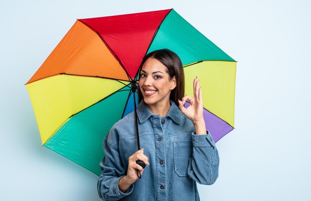 Jolie femme hispanique se sentant heureuse de montrer son approbation avec le concept de parapluie de geste correct