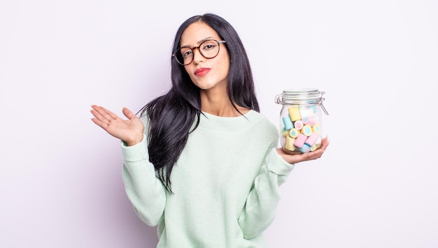 Jolie femme hispanique se sentant perplexe et confuse et doutant du concept de bonbons à la gelée