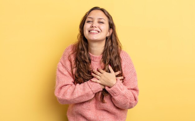 Jolie femme hispanique se sentant romantique, heureuse et amoureuse, souriant joyeusement et se tenant la main près du cœur