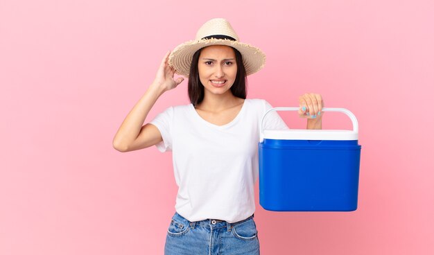 Jolie femme hispanique se sentant stressée, anxieuse ou effrayée, les mains sur la tête et tenant un réfrigérateur portable