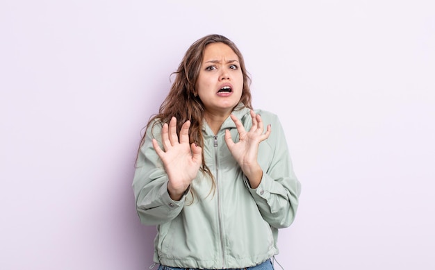 Jolie femme hispanique se sentant stupéfaite et effrayée, craignant quelque chose d'effrayant, les mains ouvertes à l'avant disant de rester à l'écart