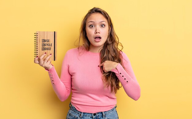 Jolie femme hispanique semblant choquée et surprise avec la bouche grande ouverte, pointant vers soi. concept de recyclage