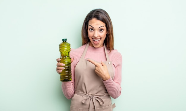 Jolie femme hispanique semblant excitée et surprise en pointant sur le côté. concept d'huile d'olive