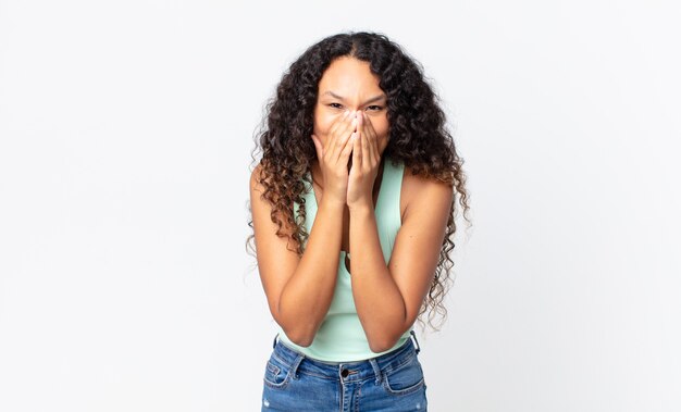 Jolie femme hispanique semblant heureuse, gaie, chanceuse et surprise couvrant la bouche avec les deux mains