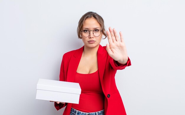 Photo jolie femme hispanique semblant sérieuse montrant la paume ouverte faisant un geste d'arrêt. concept de produit d'emballage