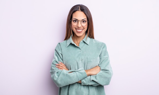 Jolie femme hispanique souriant à la caméra avec les bras croisés et une expression heureuse, confiante et satisfaite, vue latérale