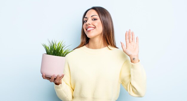 Jolie femme hispanique souriant joyeusement, agitant la main, vous accueillant et vous saluant. concept de plante d'intérieur