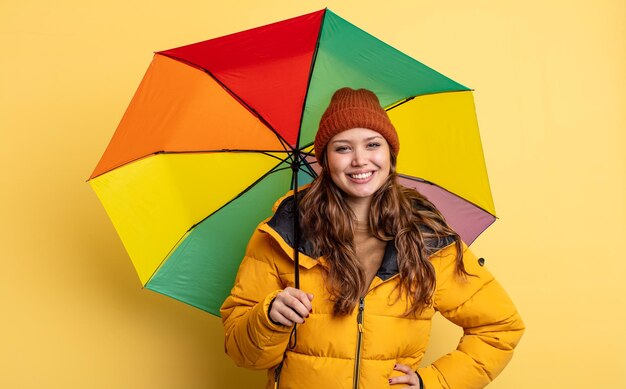 Jolie femme hispanique souriant joyeusement avec une main sur la hanche et confiante. concept de parapluie