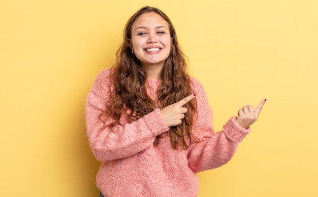 Jolie femme hispanique souriant joyeusement et pointant vers le côté et vers le haut avec les deux mains montrant l'objet dans l'espace de copie