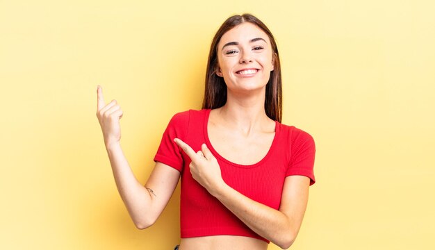 Jolie femme hispanique souriant joyeusement et pointant vers le côté et vers le haut avec les deux mains montrant l'objet dans l'espace de copie