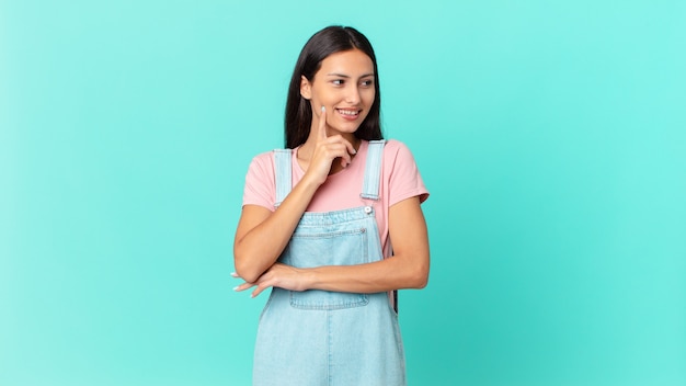 Jolie femme hispanique souriant joyeusement et rêvant ou doutant