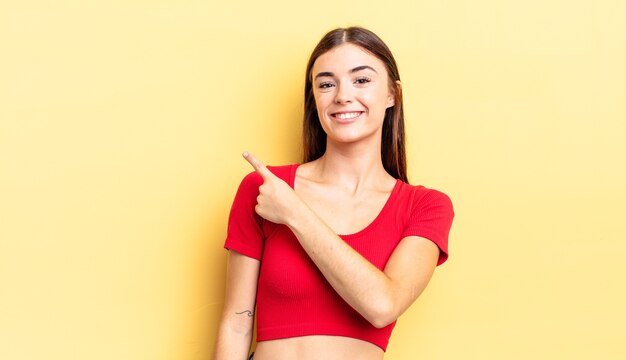 Jolie femme hispanique souriant joyeusement, se sentant heureuse et pointant vers le côté et vers le haut, montrant l'objet dans l'espace de copie