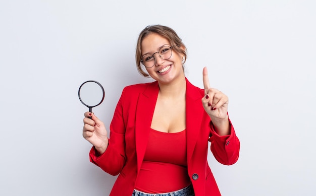 Jolie femme hispanique souriante et amicale montrant le concept de loupe numéro un