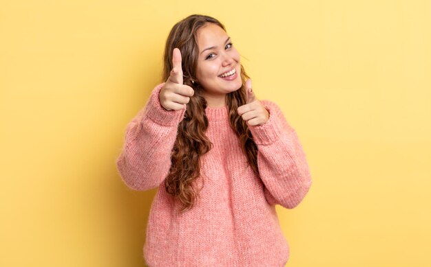 Jolie femme hispanique souriante avec une attitude positive, réussie et heureuse pointant vers la caméra, faisant un signe d'arme avec les mains