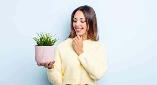 Jolie femme hispanique souriante avec une expression heureuse et confiante avec la main sur le menton. concept de plante d'intérieur