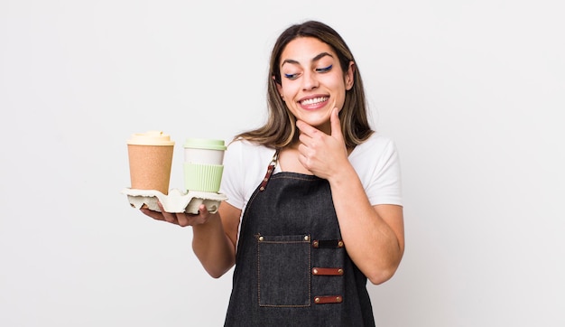 Jolie femme hispanique souriante avec une expression heureuse et confiante avec la main sur le menton à emporter concept de café