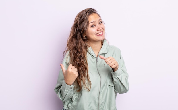 Jolie femme hispanique souriante joyeusement et désinvolte pointant vers l'espace de copie sur le côté, se sentant heureuse et satisfaite