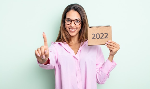 Jolie femme hispanique souriante et semblant amicale, montrant le numéro un. concept de calendrier 2022