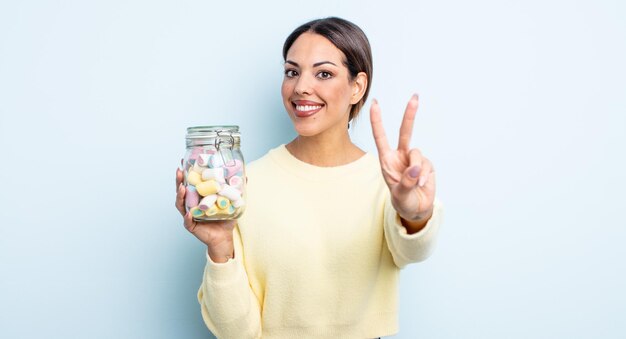 Jolie femme hispanique souriante et semblant amicale, montrant le numéro deux. concept de bonbons à la gelée