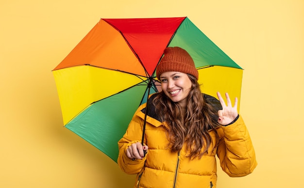 Jolie femme hispanique souriante et semblant amicale, montrant le numéro trois. concept de parapluie