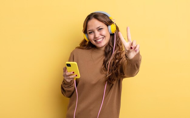 Jolie femme hispanique souriante et semblant heureuse, gesticulant la victoire ou la paix. casque et concept de smartphone