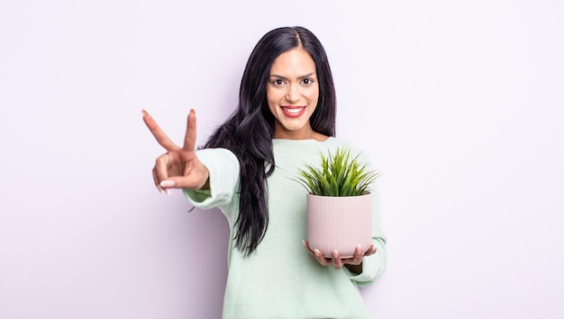 Jolie femme hispanique souriante et semblant heureuse, gesticulant la victoire ou la paix. concept de plante d'intérieur